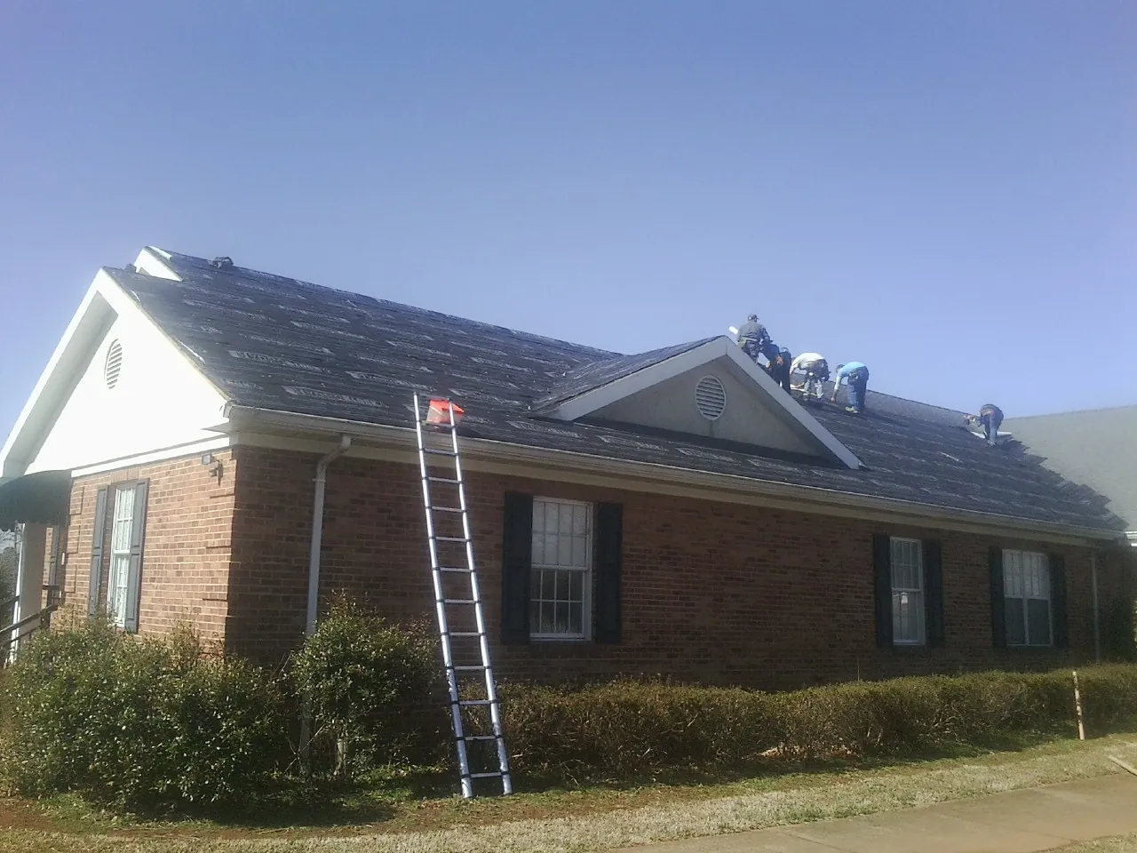 Crew tearing shingles off a brick ranch roof with a ladder set — Metal Roof Repair work by our crew in Fishs Eddy