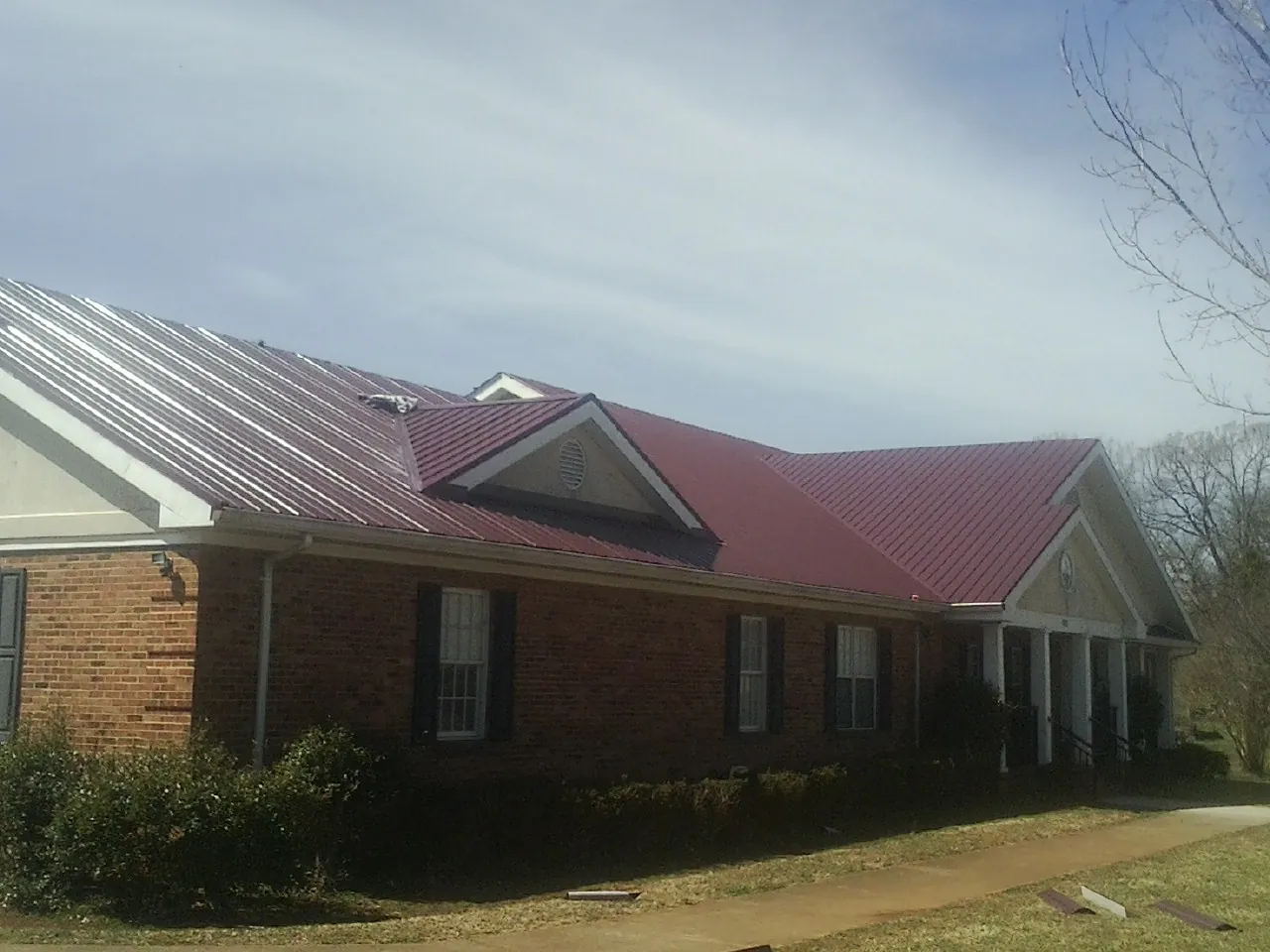 Red metal roof with gabled entries on a long brick building, from a Hail Damage Roof Repair job in Fishs Eddy