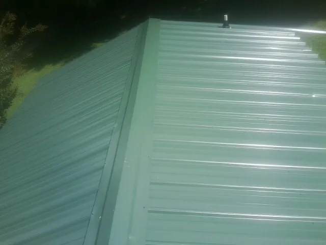 New green metal panels meeting at the ridge of a roof — Flat Roof Repair work by our crew in Fishs Eddy