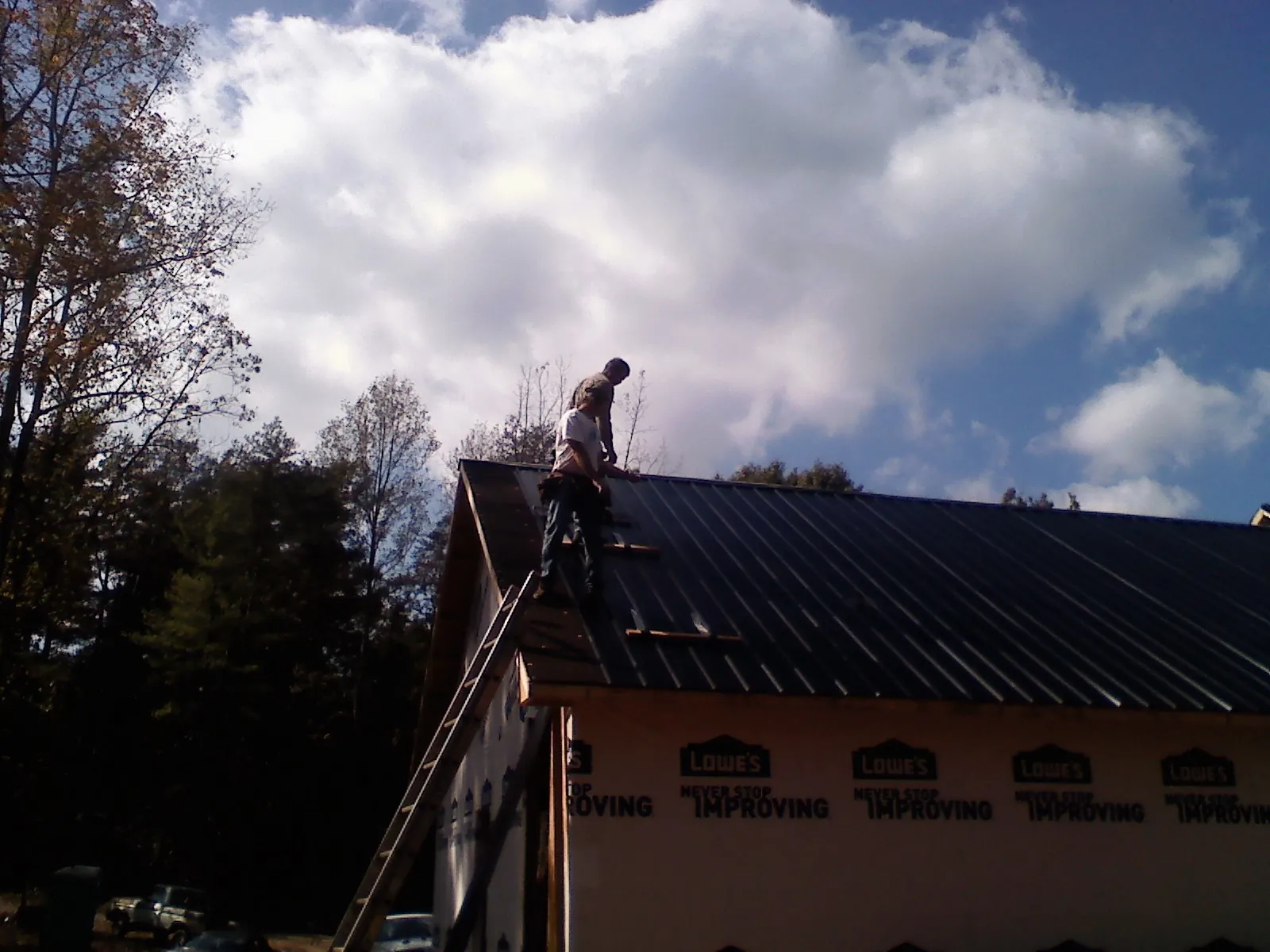 Roofer fastening dark metal panels high against a cloudy sky, from a Roof Inspection job in Fishs Eddy