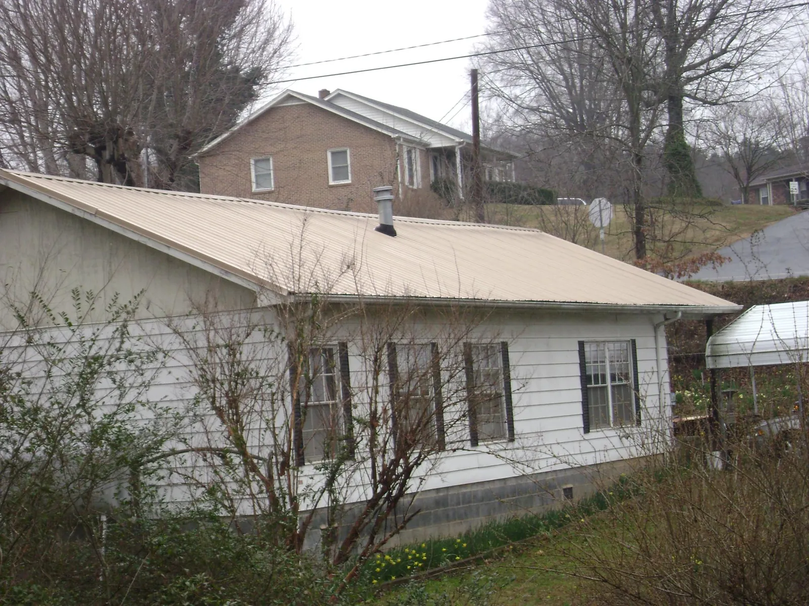 Tan metal roof on a white sided house set into a hillside — Commercial Roofing by Roofing Brothers in Fishs Eddy